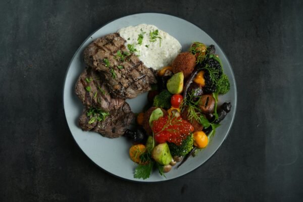 A top view of grilled beef steak with mixed vegetables and sauce on a plate.