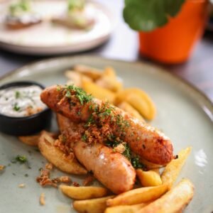 Close-up of juicy sausages with fries and sauce on a plate. Perfect for food lovers.