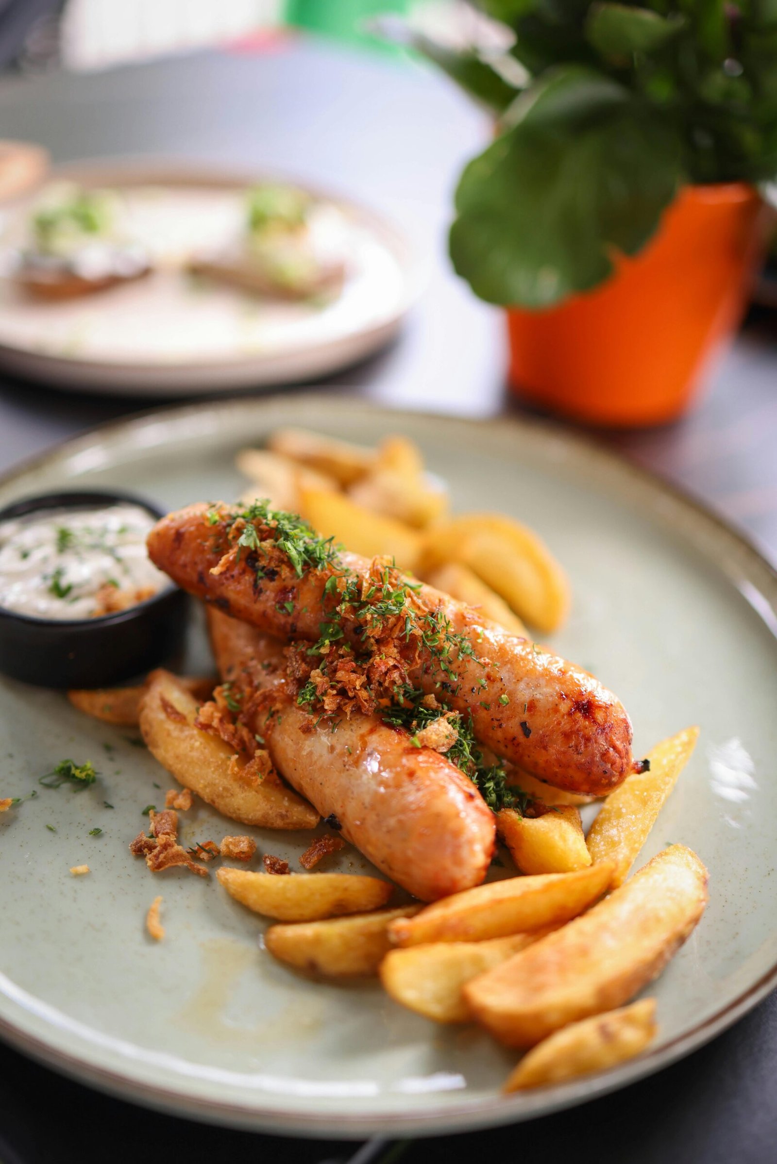 Close-up of juicy sausages with fries and sauce on a plate. Perfect for food lovers.