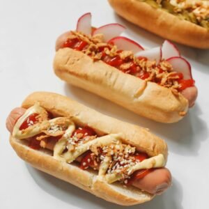 Three gourmet hot dogs topped with mustard, ketchup, and fresh vegetables on a white background.